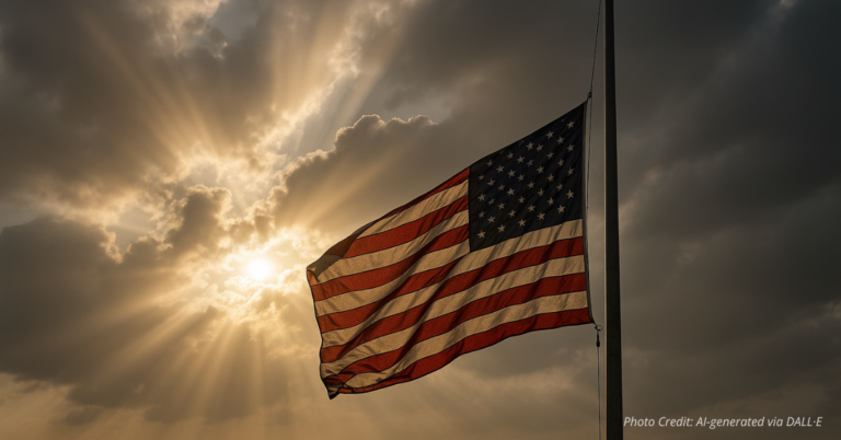 American flag at half-staff with sunlight breaking through clouds