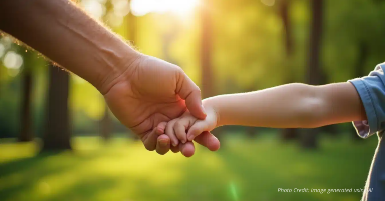 Father’s hand holding child’s hand outdoors.