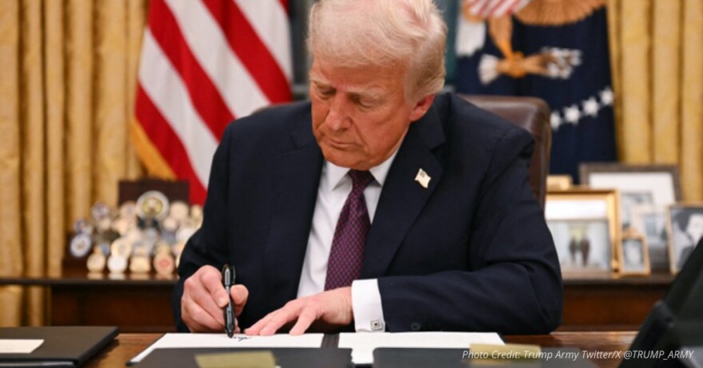 Donald Trump signs executive order at desk with U.S. flag in background