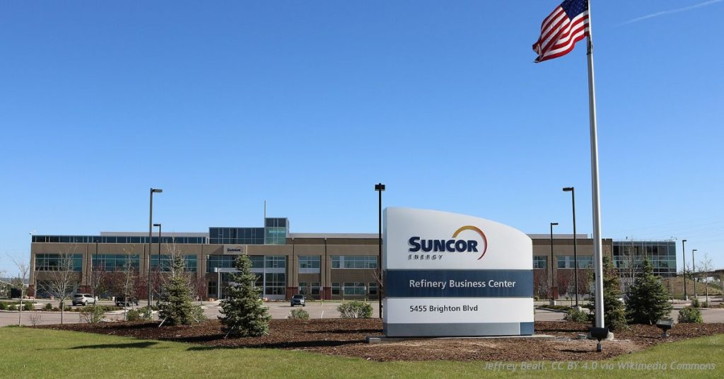 Suncor Energy Refinery Business Center building and sign under a clear blue sky with a U.S. flag.